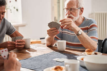 Senior man playing at the cards with his friends while sitting at the tableの写真素材