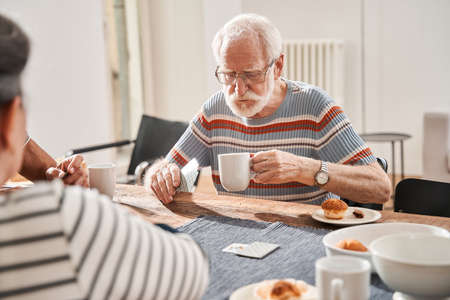 Senior man holding cup of tea and playing at the cardsの写真素材