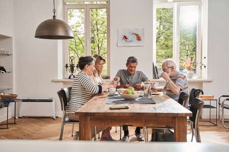 Pensioners sitting at the table with their caregiver and playing at the cardsの写真素材