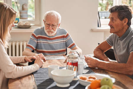 Two senior man sitting at the table with their caregiver and chatting