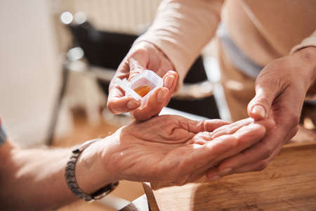 Caregiver pulling pills at the palm to senior man while working at the nurse houseの写真素材