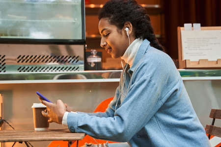 Woman wearing earphones browsing internet or chatting with somebody while resting