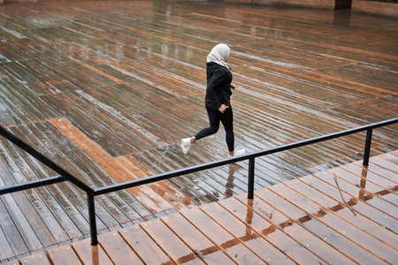 Fitness woman dressed in hijab and dark clothes running outdoors at the street by stepsの写真素材