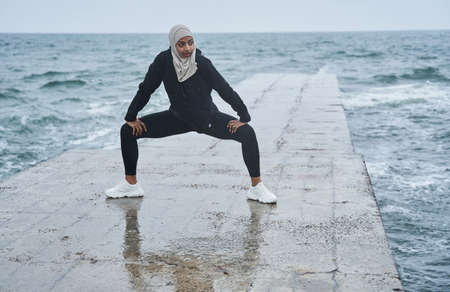 Woman doing squats while training at the open air at the pierの写真素材