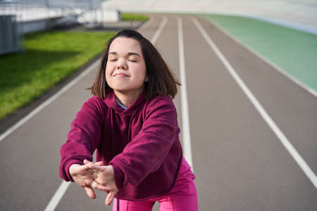 Midget girl is warming up at the stadium and stretching her hands before the trainingの写真素材