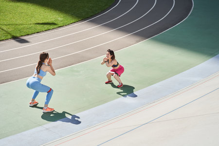 Smiling girls in sport uniform squats and stretches at the stadium