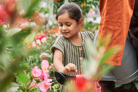 Botanist holding a watering can with one hand while her granddaughter helping
