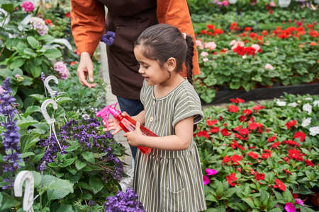 Girl holding plastic bottle and spraying with water at the flowers