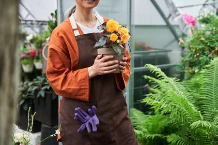Florist holding plant with soil at the pot at her hands while standing and smilingの写真素材