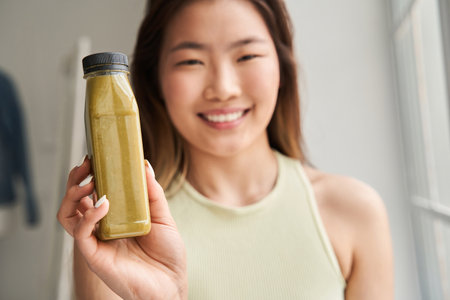 Laughing young woman showing to the camera fruit or vegetable smoothie