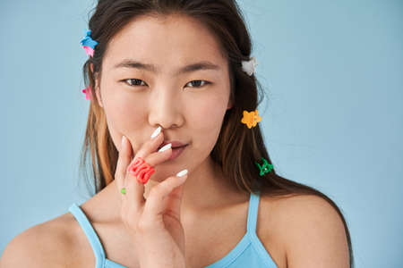 Woman with cute hairpins at her brunette hair posing with blue wall at the background