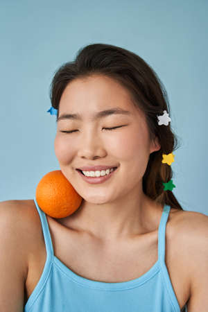 Woman posing at the camera with closed eyes and orange at her shoulderの写真素材