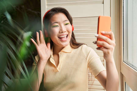 Woman wearing headphones waving to the smartphone camera while chattingの写真素材