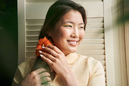 Woman straightens orange flower at her brunette hair and smilingの写真素材