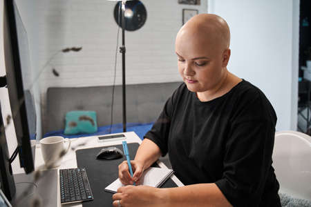Bald woman wearing domestic clothes looking concentrated while making notesの写真素材