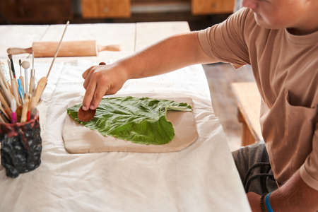Boy with down syndrome putting green leaf at the clay and impressing texture of it