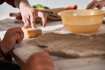Sculptor sitting at the table with boy with special needs and explaining to him