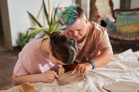 Boy with colored hair helping to his girlfriend sculpting from clay during master class