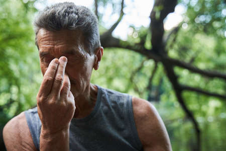 Senior man practicing breathing yoga pranayama while sitting at the mat outdoors