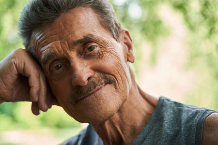 Man looking at the camera with pleasure smile while leaning at the trunk of the tree