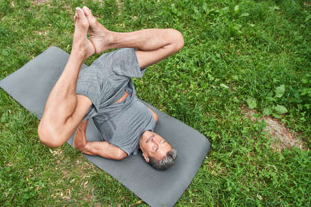 Man holding his body with hands while laying at the yoga mat and doing gymnastic exercises
