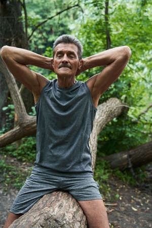 Man with closed eyes keeping his hands behind the head and sitting at the tree