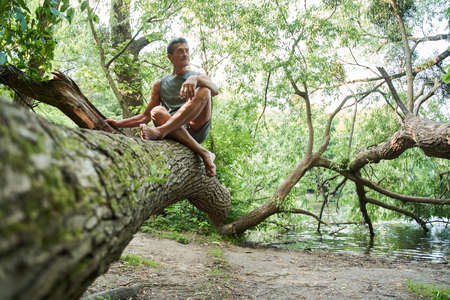 Man sitting at the tree trunk and looking away while relaxing at the natureの写真素材