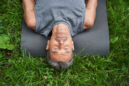 Man laying at the yoga mat at the grass after exercises and relaxingの写真素材