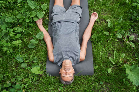 Man laying on sport mat, relaxing in savasana pose after exercising at the fresh air