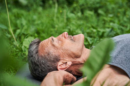 Mature man doing relaxing yoga pose while laying on the mat at the natureの写真素材