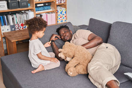 Man laying at the sofa with his daughter and looking at each other with tenderness