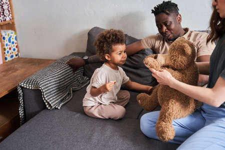 Curly girl looking at her lovely teddy bear while her mother holding himの写真素材