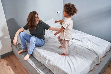 Mother sitting at the bed and listening her cute daughter while spending morning togetherの写真素材