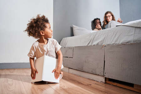 Girl sitting at the floor at the bedroom and looking at her parents while playingの写真素材
