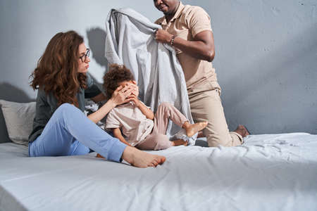 Diverse parents and their female kid sitting at the bed an playing at the funny gameの写真素材