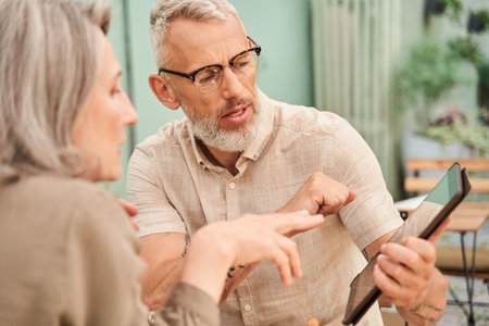 Woman looking at the tablet screen while her husband telling something to herの写真素材