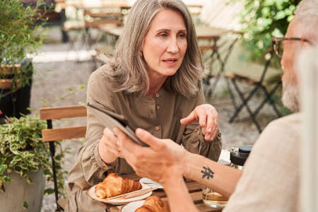 Woman telling something seriously to her husband while he holding tabletの写真素材