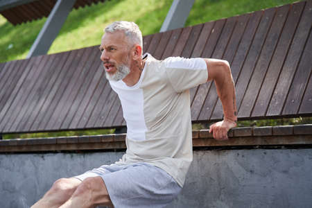 Senior tired and concentrated man making squats and holding at the benchの写真素材