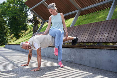 Man making push ups and holding legs at the bench while his wife leaning at his back