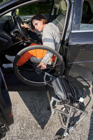 Handicapped car driver sitting at the front seat and transporting her wheelchair insideの写真素材