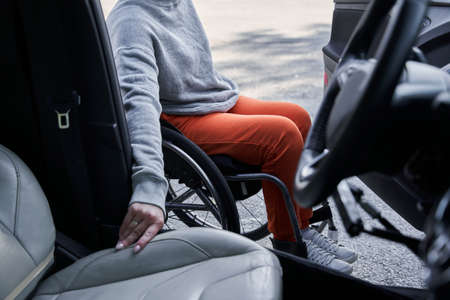 Young disabled female getting out from the car in her wheelchair after the roadの写真素材