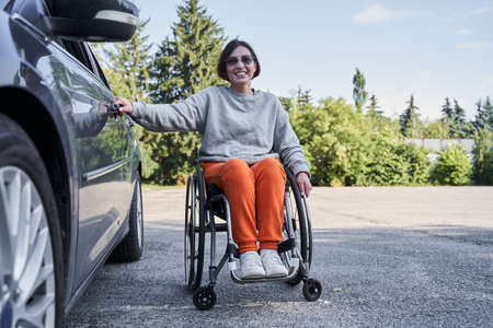 Disabled woman on wheelchair boarding a car door during the sunny dayの写真素材
