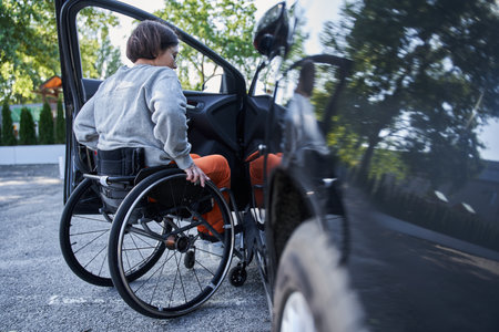 Young girl with lower body disability switches position from the wheelchair into the carの写真素材