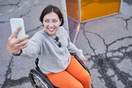 Disabled woman making selfie while sitting at the wheelchair during the walkingの写真素材