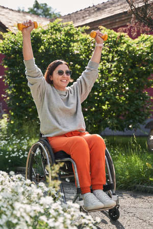 Handicapped woman holding dumbbells and training at the fresh air around the treesの写真素材