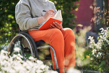 Girl with loss of leg function sitting at the wheelchair and making notesの写真素材
