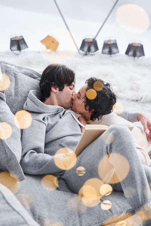 Man kissing his woman while both relaxing on the sofa after reading
