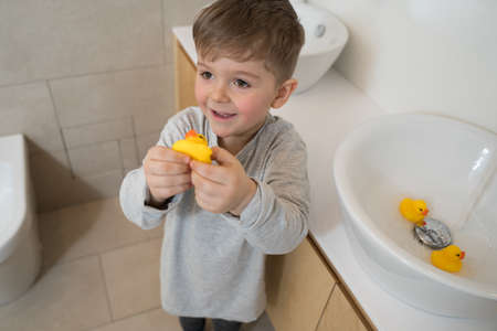 Boy playing with his rubber ducks at the bathroomの写真素材