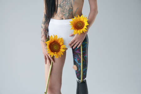 Tattooed girl with prothesis leg holding sunflowers in front of the white backgroundの写真素材