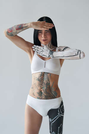Vertical shot of women with painted hand of robot body art. Woman posing at the studio and holding her hands near her face. White wall at the backgroundの写真素材